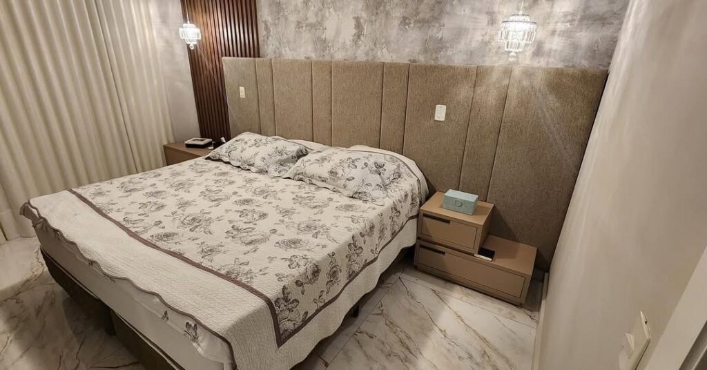Detalhe de acabamento de cabeceira de cama de luxo com logomarca da Magnífico Estofados. Imagem demonstra a precisão na tapeçaria modular e o uso de materiais de alta qualidade para dormitórios de alto padrão.
