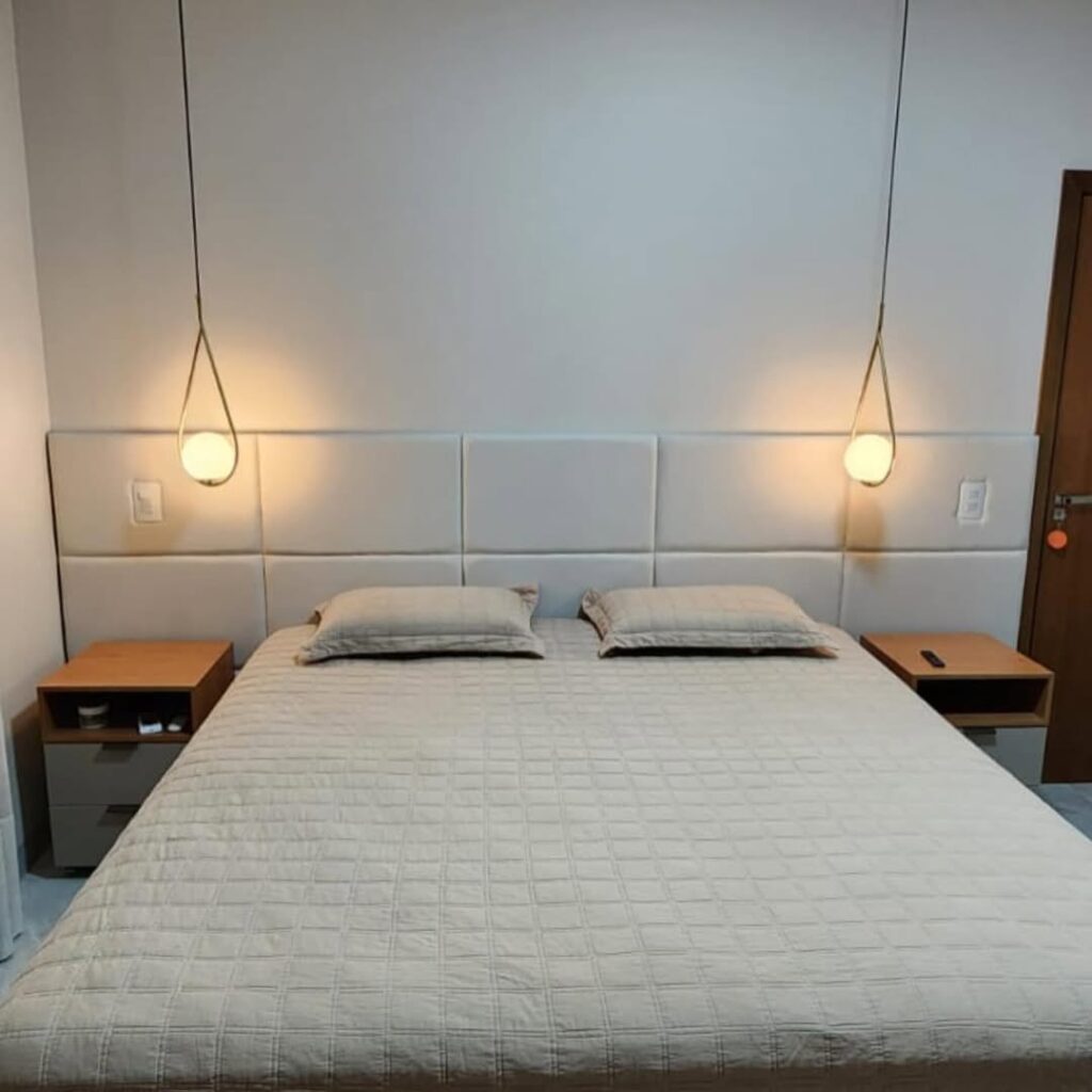 Cabeceira de cama modular na cor branca com acabamento em gomos, fabricada sob medida. Detalhe de quarto de casal com iluminação pendente, destacando o trabalho de estofaria fina e materiais de alta resiliência.